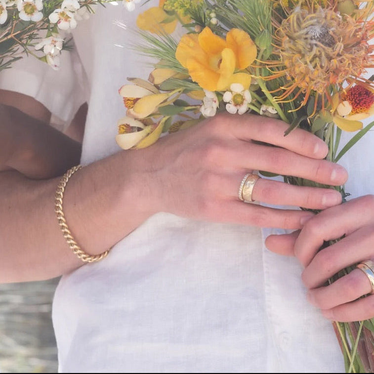 Person holding a bouquet of flowers with gold jewelry